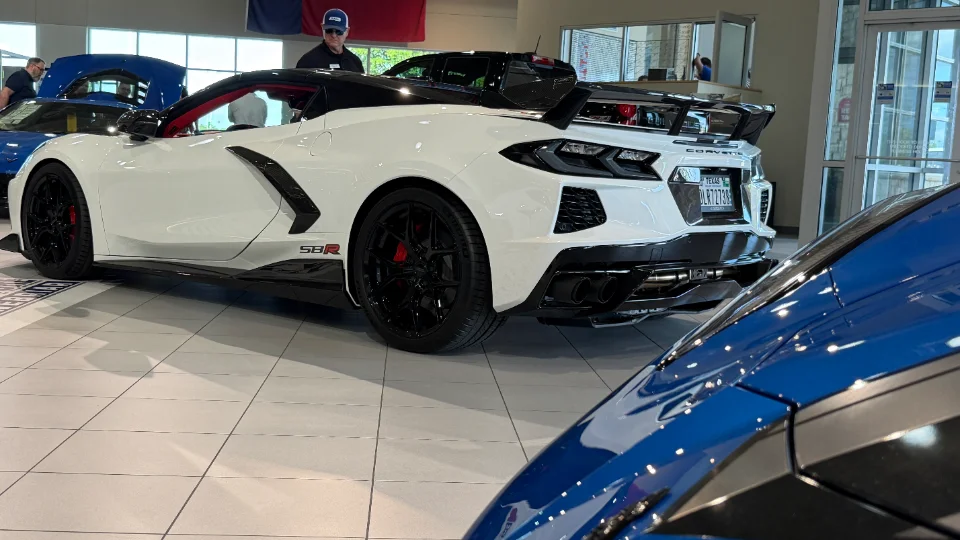White C8 Corvette with a large rear wing and black wheels displayed in a showroom.