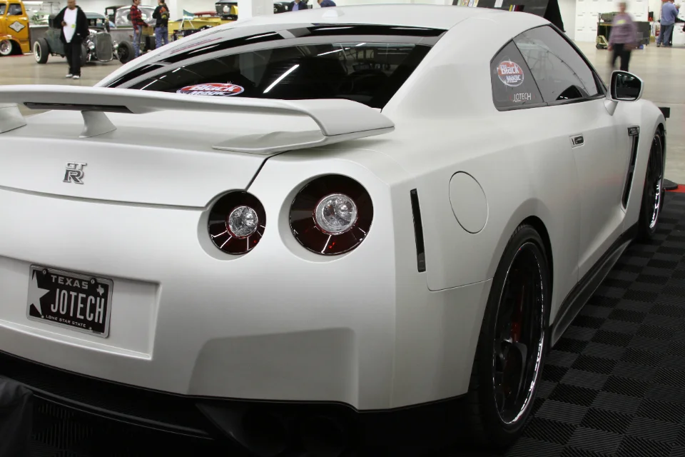 A white Nissan GT-R R35 with a Jotech license plate and window sticker, displayed at an indoor car show.