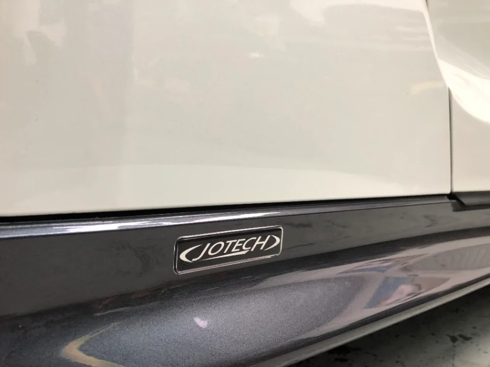 Close-up of a Jotech badge on the side skirt of a white performance car.