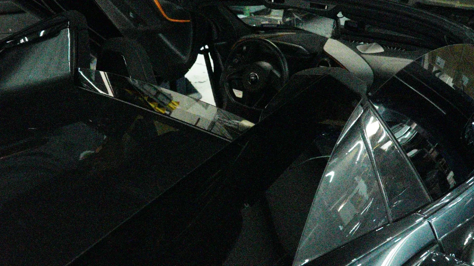 Overhead view of a dark McLaren's interior, showing the steering wheel and dashboard, parked inside a shop.