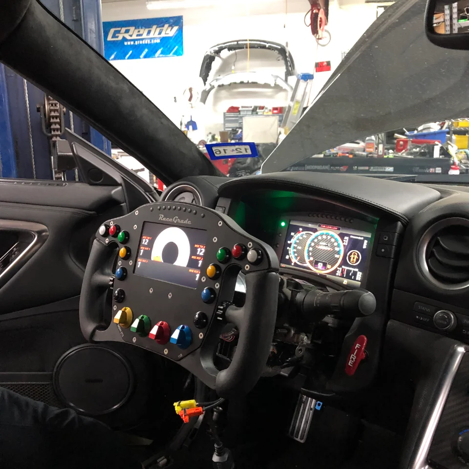 Interior view of a Nissan GT-R in a shop, featuring a RaceGrade custom steering wheel and digital dashboard.