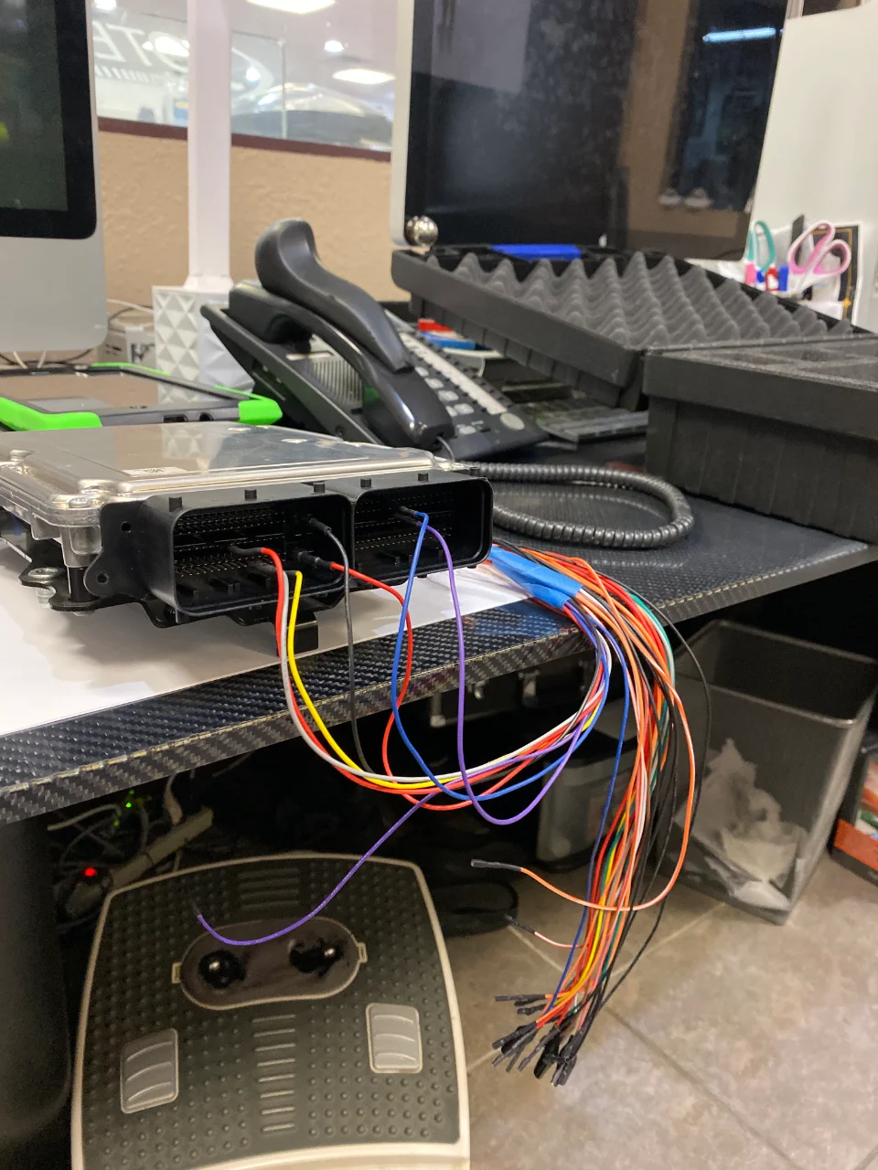 An ECU with a complex wiring harness connected, sitting on a desk in a performance tuning shop.
