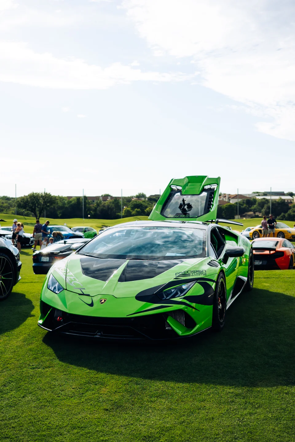 A bright green Lamborghini Huracan with black accents and "Precision Turbo" livery parked on a grassy field at a car show.