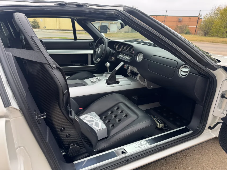 Interior view of a white Ford GT, showcasing the carbon fiber backed driver's seat, dashboard, and door sill.