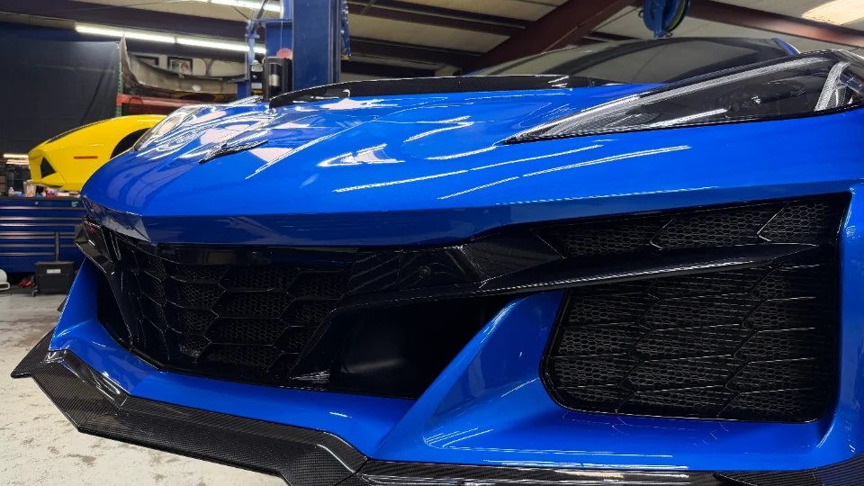 Front view of a blue C8 Corvette Z06 with a carbon fiber splitter in a performance shop.