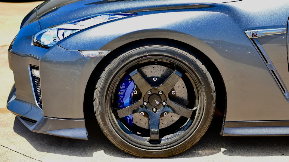 Close-up of a grey Nissan GT-R R35's front wheel, featuring black multi-spoke wheels and blue brake calipers.