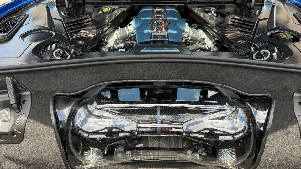 A detailed view of a blue Corvette C8 mid-engine bay with carbon fiber accents and a custom blue engine cover.