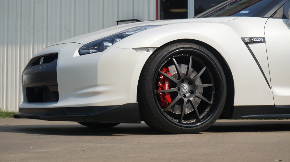 White Nissan GT-R with custom dark wheels, red Brembo brake calipers, and a front splitter.