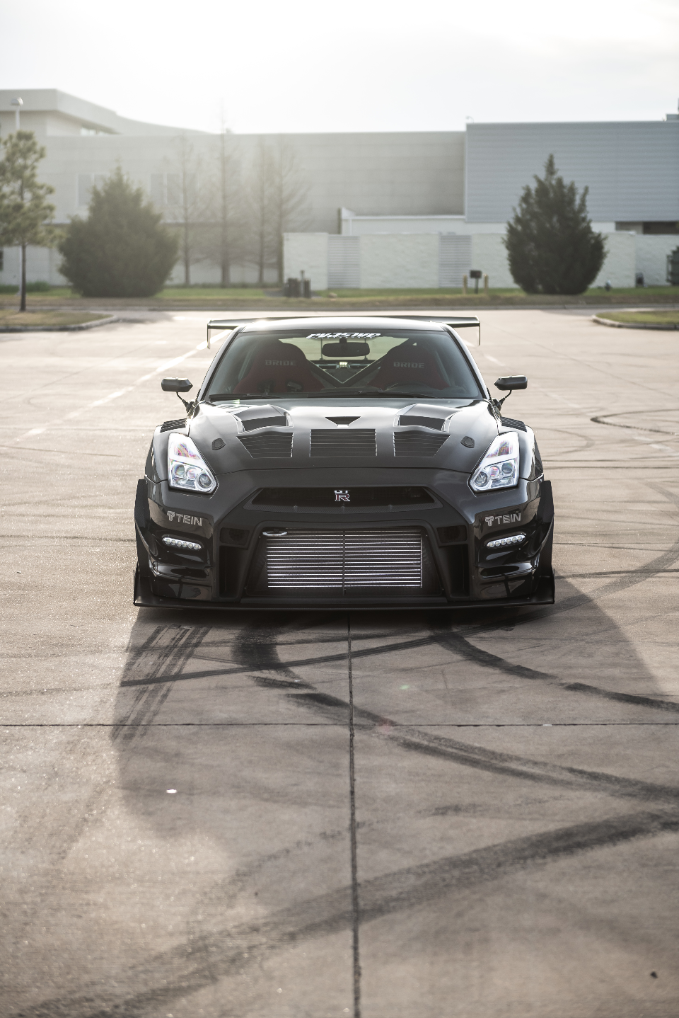 A black widebody Nissan GT-R R35 with a large front-mount intercooler and rear wing parked in a lot with tire marks.