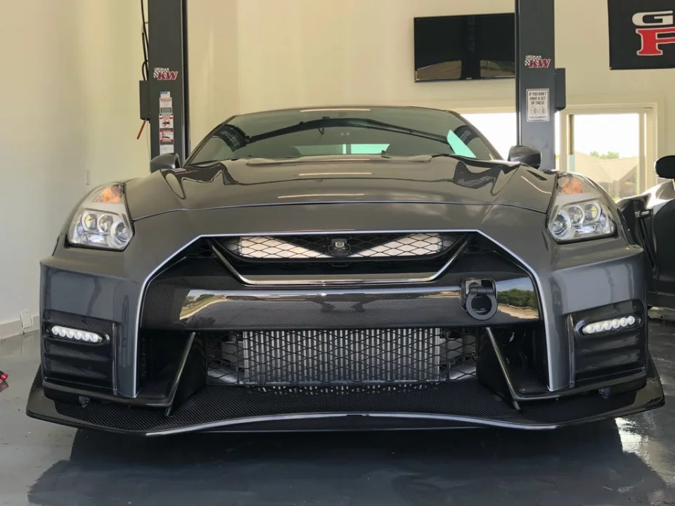 Front view of a grey Nissan GT-R with an aftermarket carbon fiber front bumper and splitter in a shop.