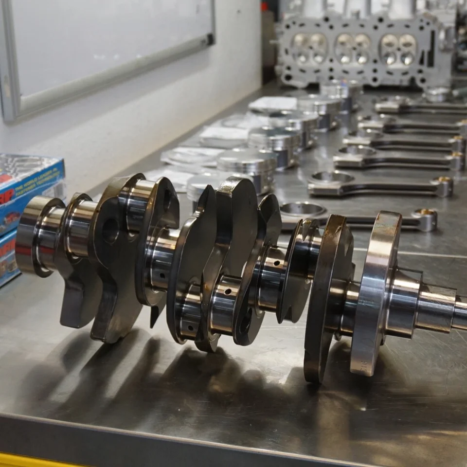 Crankshaft, pistons, connecting rods, and cylinder head laid out on a workbench for an engine build at Jotech Motorsports.