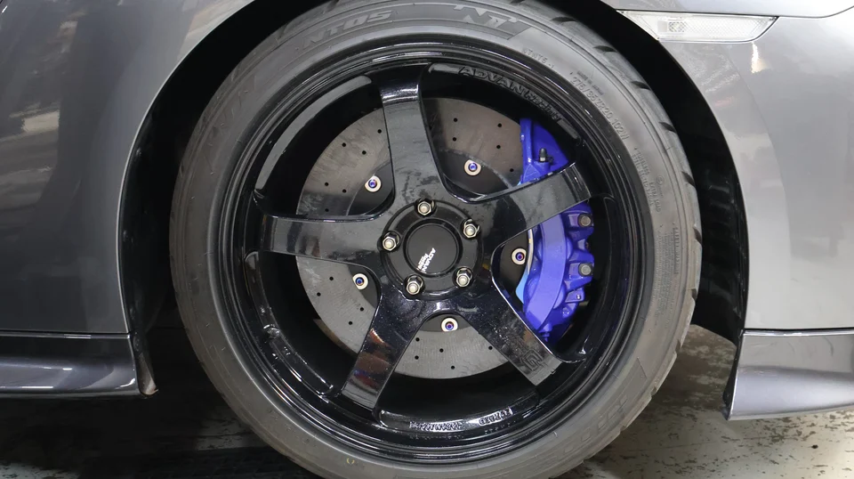 A close-up of a grey car's black Advan wheels with blue brake calipers and Nitto tires.