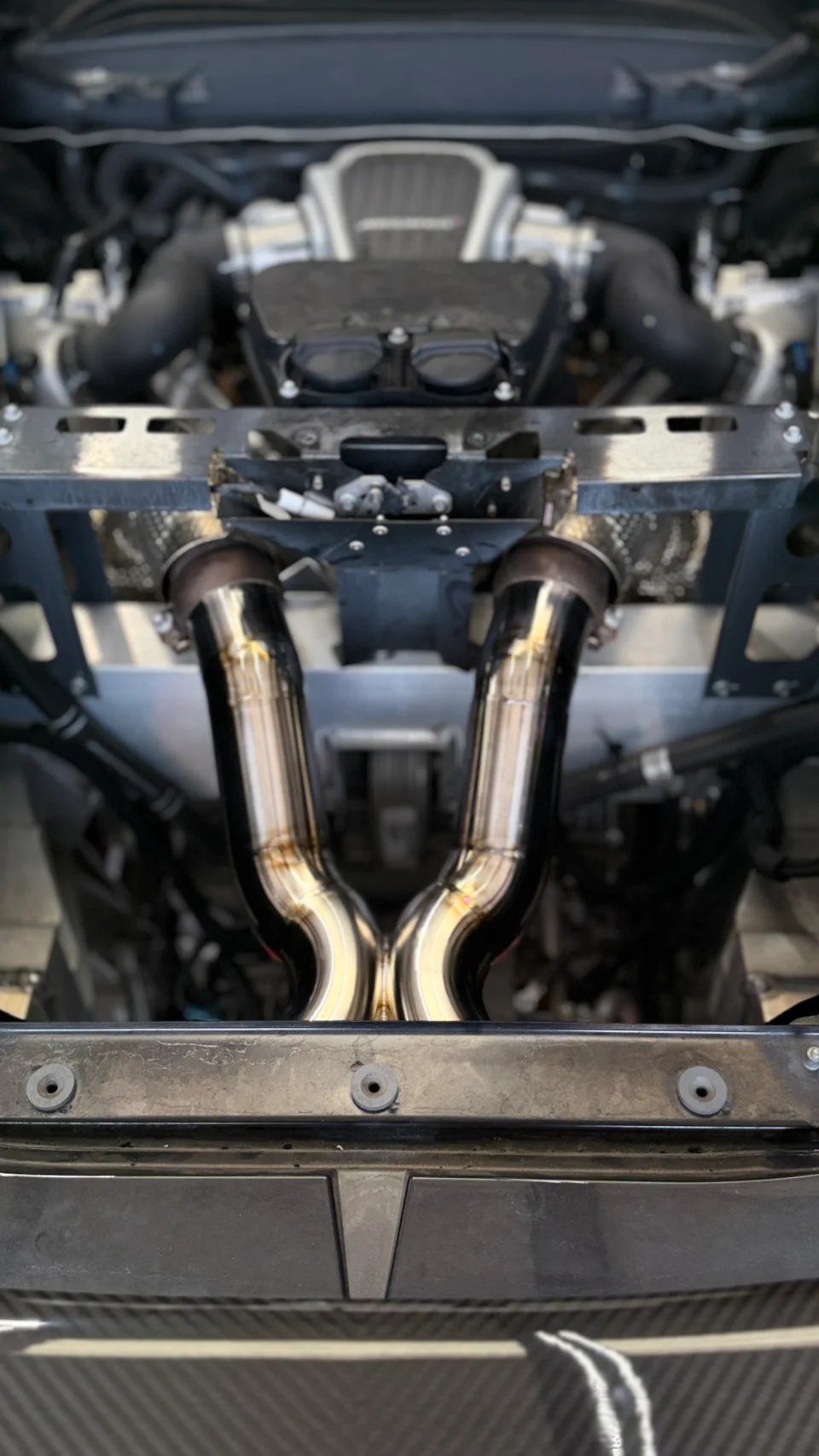Close-up view of polished aftermarket exhaust downpipes installed in a high-performance car's engine bay.