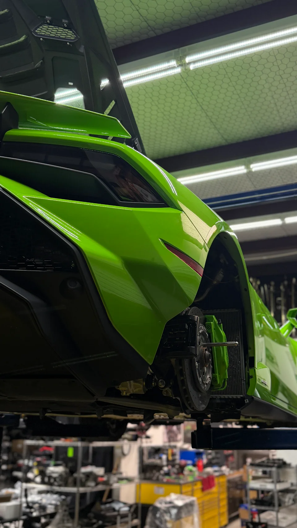 Green Lamborghini Huracan on a lift in a performance shop, with the rear wheel removed exposing the brake system.