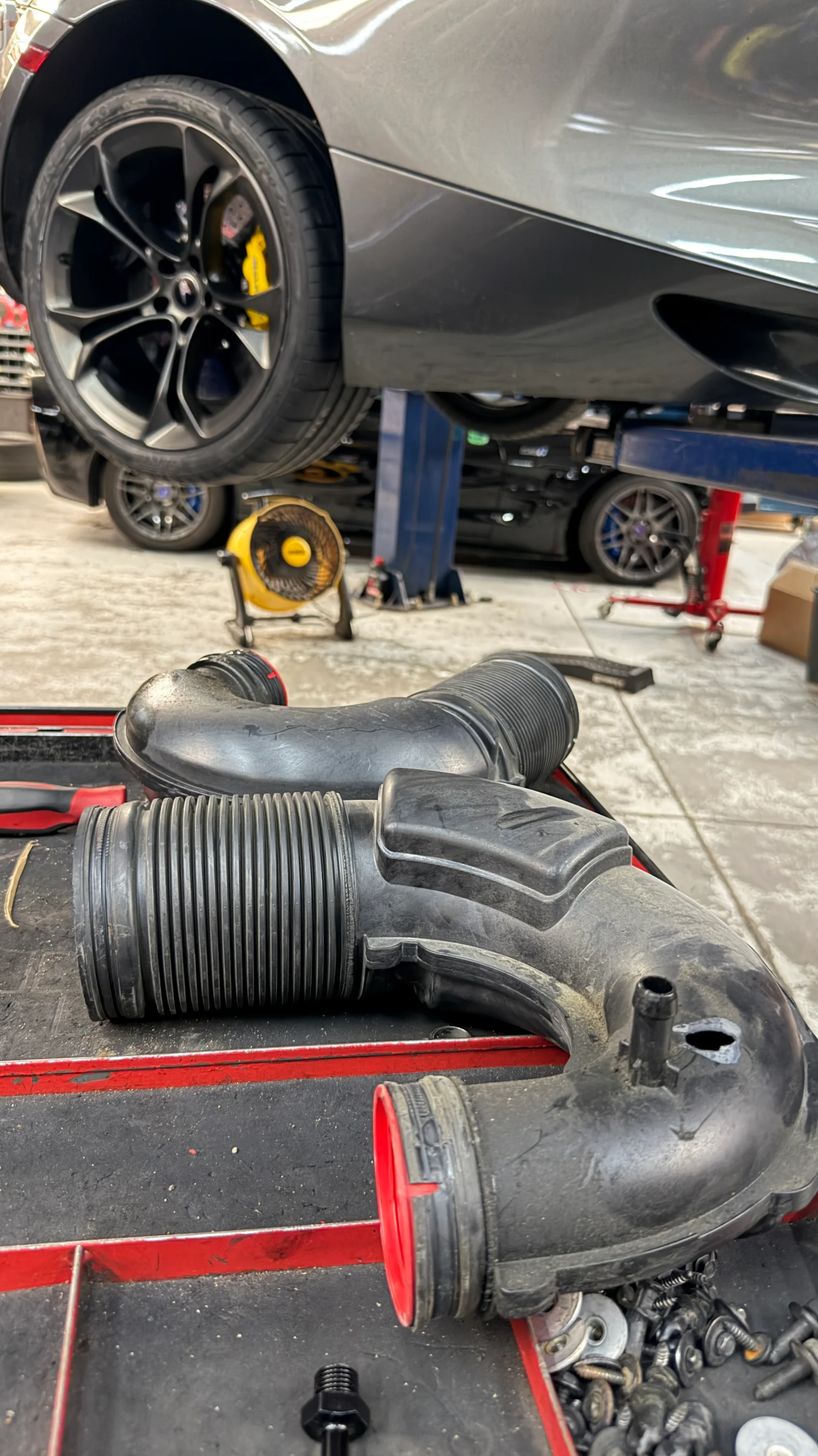 OEM intake tubes on a workbench in a performance shop with a McLaren on a lift in the background.