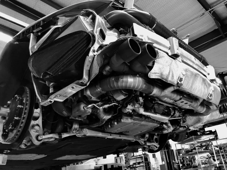 Black and white photo of the underside of a Porsche on a lift, showcasing the aftermarket exhaust system and turbochargers.