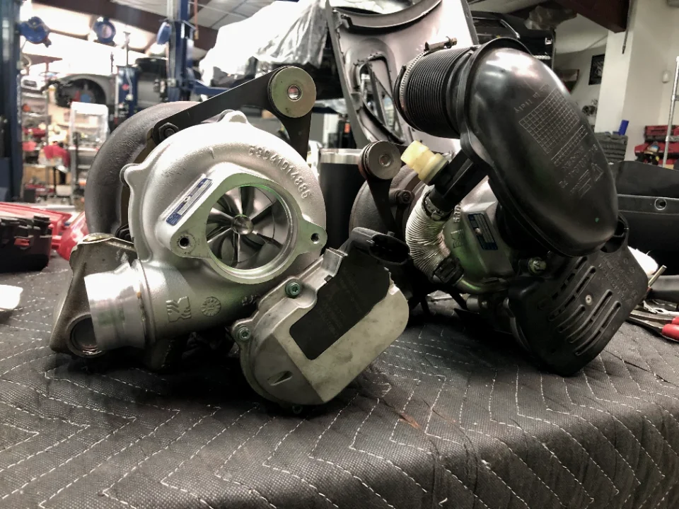 Two turbochargers, one with a visible compressor wheel, on a workbench in a performance tuning shop.