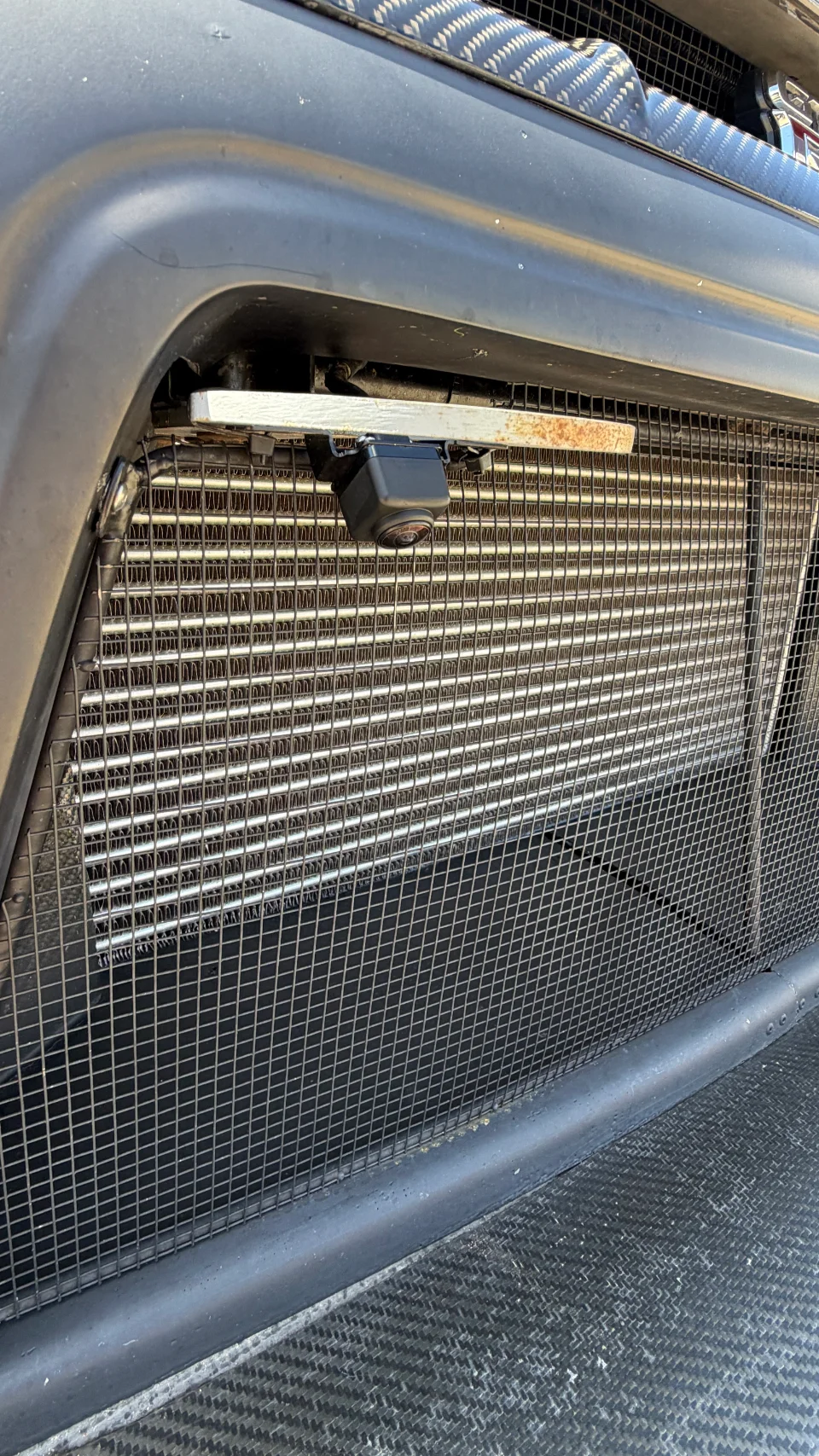 Close-up of a car's front grille showing an intercooler, front-mounted camera, and carbon fiber bodywork.