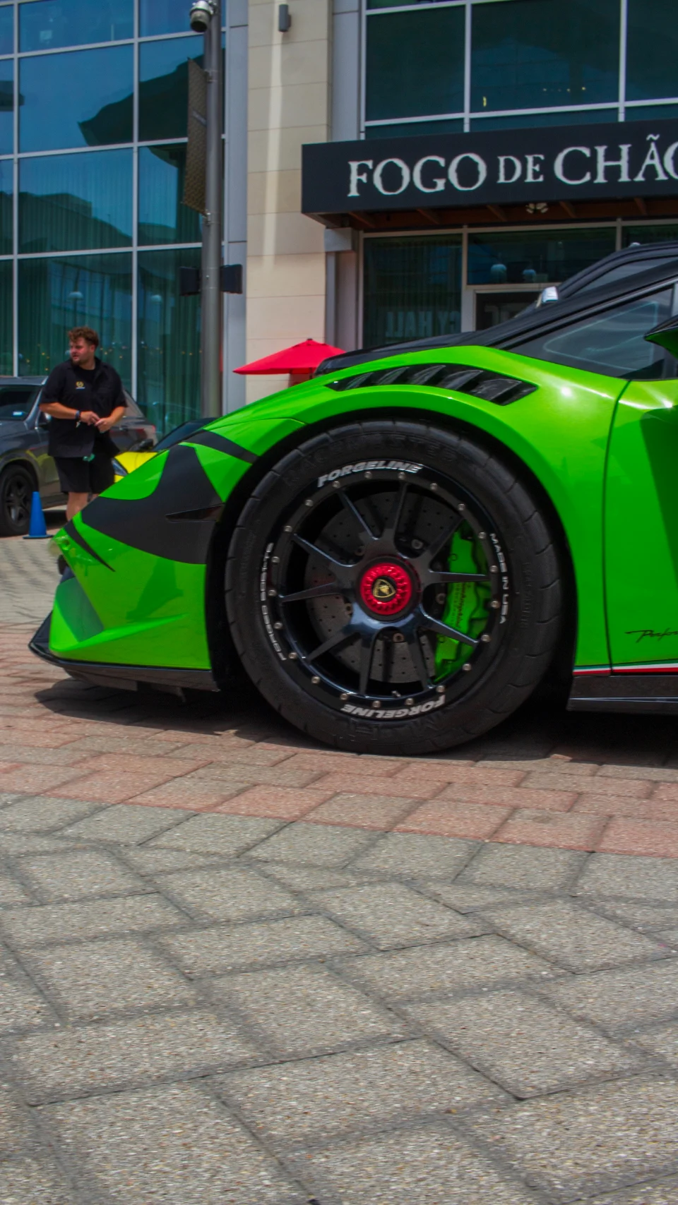 A close-up of a bright green Lamborghini with black Forgeline wheels and green brake calipers, parked outside a building.
