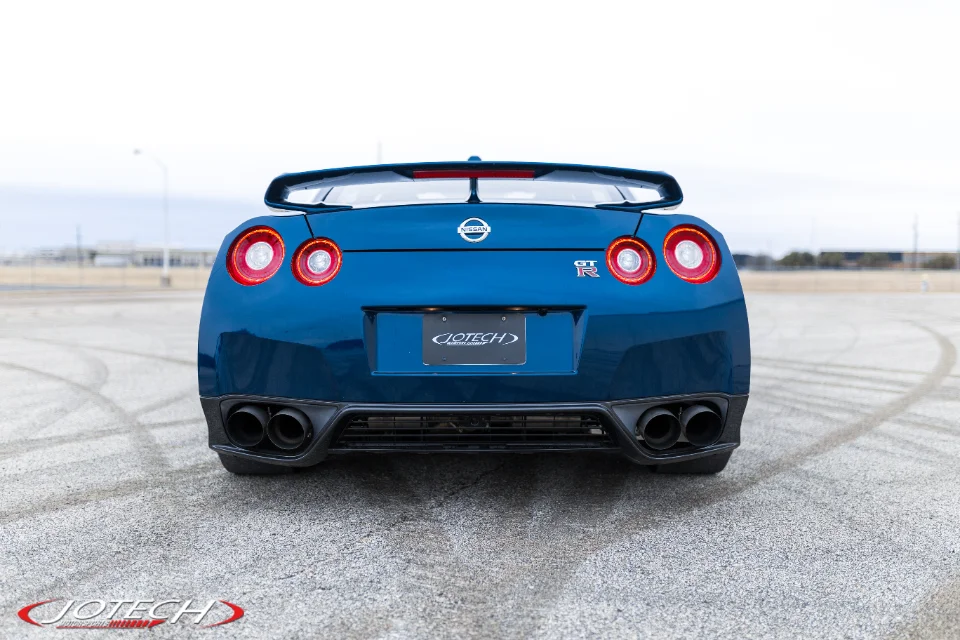 Rear view of a blue Nissan GT-R with quad exhaust tips, parked in an open lot.