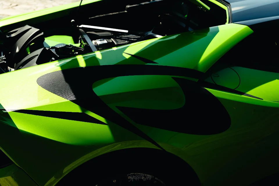 Close-up of a bright green supercar with its hood open, featuring custom black graphics and carbon fiber accents.