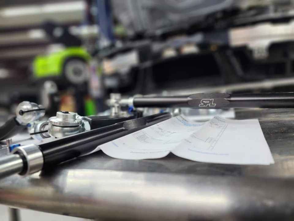 SPL Parts suspension components, including control arms and spherical bearings, laid out on a workbench in a performance shop.