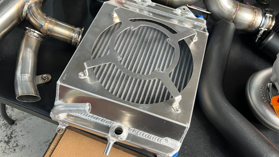 A close-up of various performance parts including an aluminum intercooler, turbocharger, and custom boost piping.