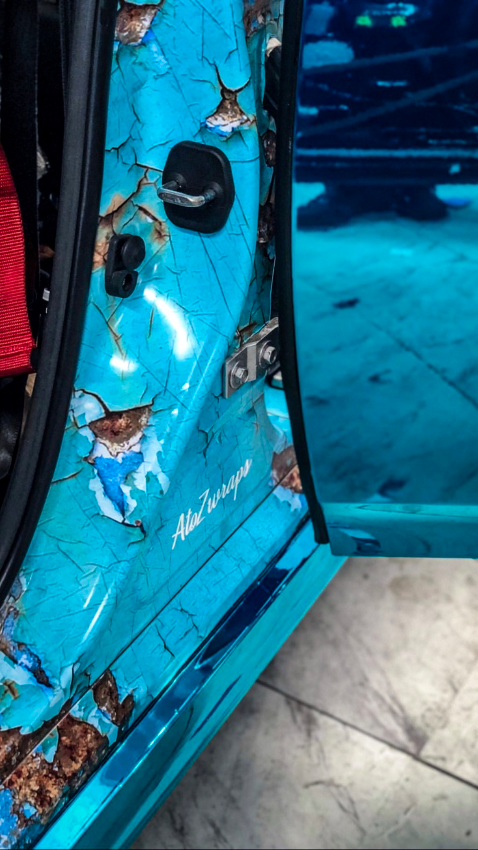 A close-up detail of a car door featuring a unique turquoise and rust-effect cracked paint wrap by AtoZwraps.