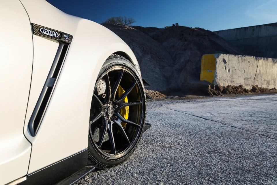 Close-up of a white Nissan GT-R's front wheel, featuring black forged wheels, yellow Brembo brake calipers, and a carbon fiber fender vent.