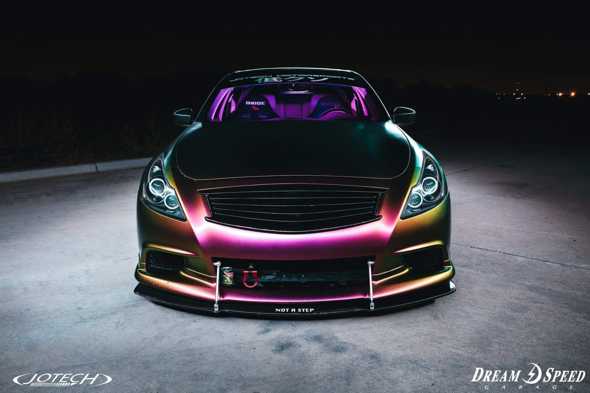 A front view of a custom Infiniti G37 coupe with a chameleon wrap, LED headlights, and purple interior lighting at night.