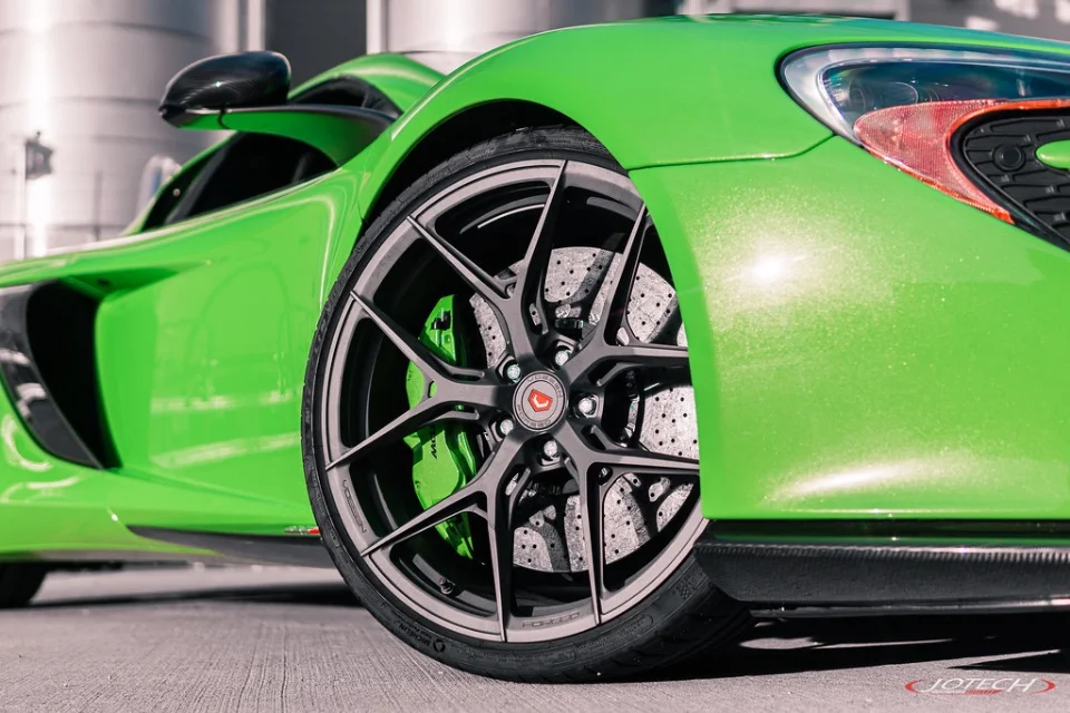 Close-up of a bright green McLaren supercar featuring custom Vossen wheels and large carbon ceramic brakes.