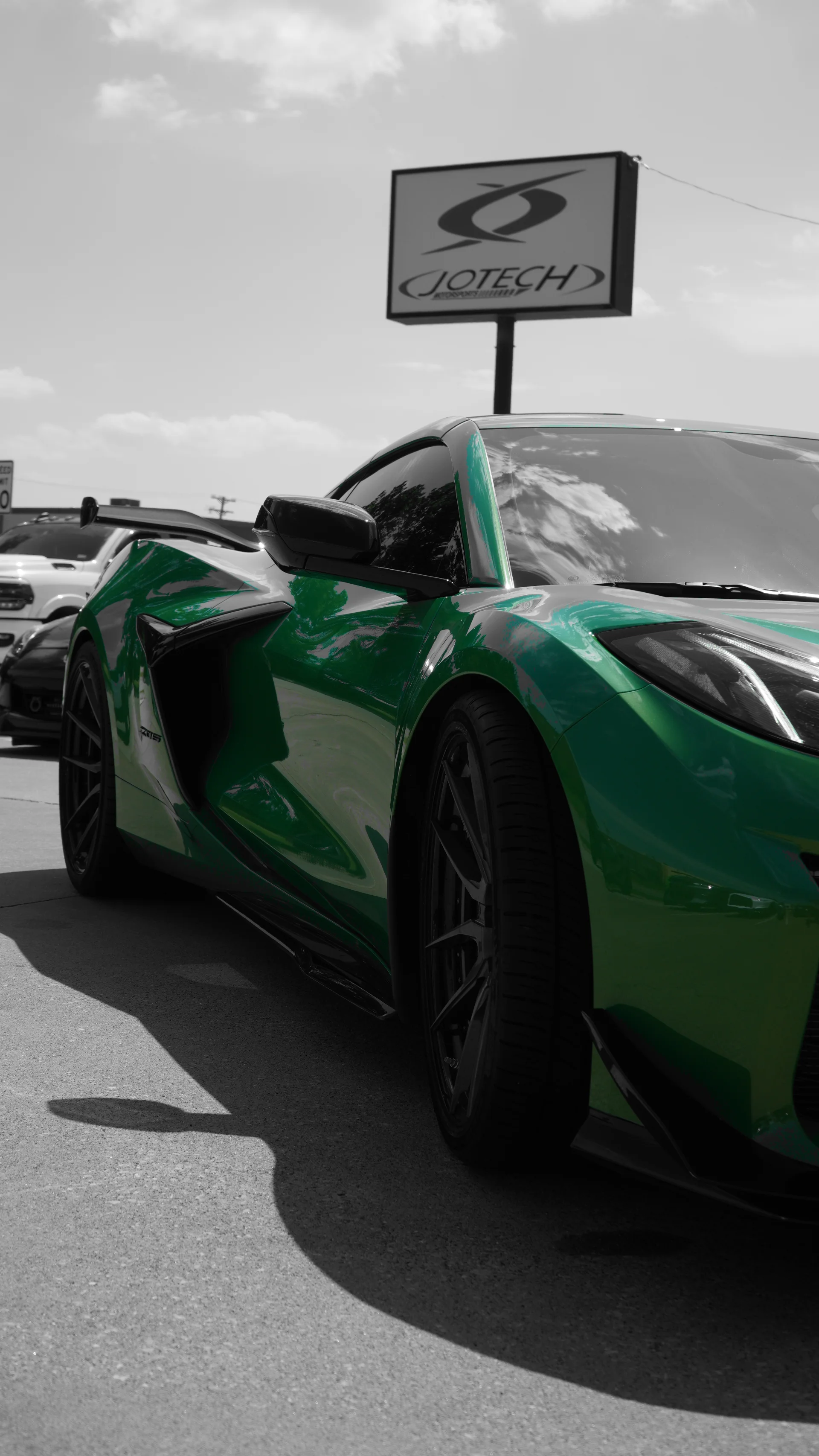 A vibrant green C8 Corvette with aftermarket wheels parked outdoors in front of a Jotech Motorsports sign.