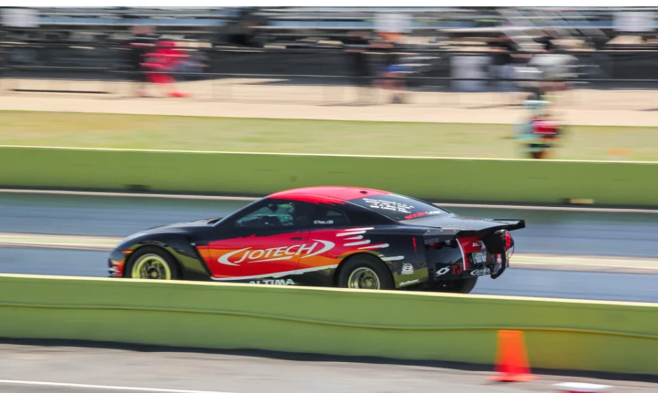 A black and red Jotech Nissan GT-R race car speeds down a drag strip with motion blur.