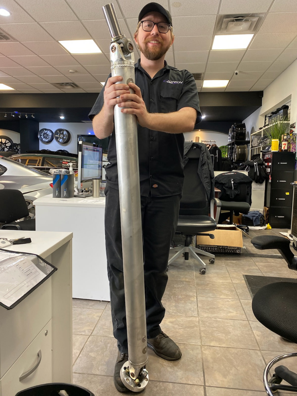 A Jotech employee holds a long, silver performance driveshaft in the Jotech Motorsports shop.
