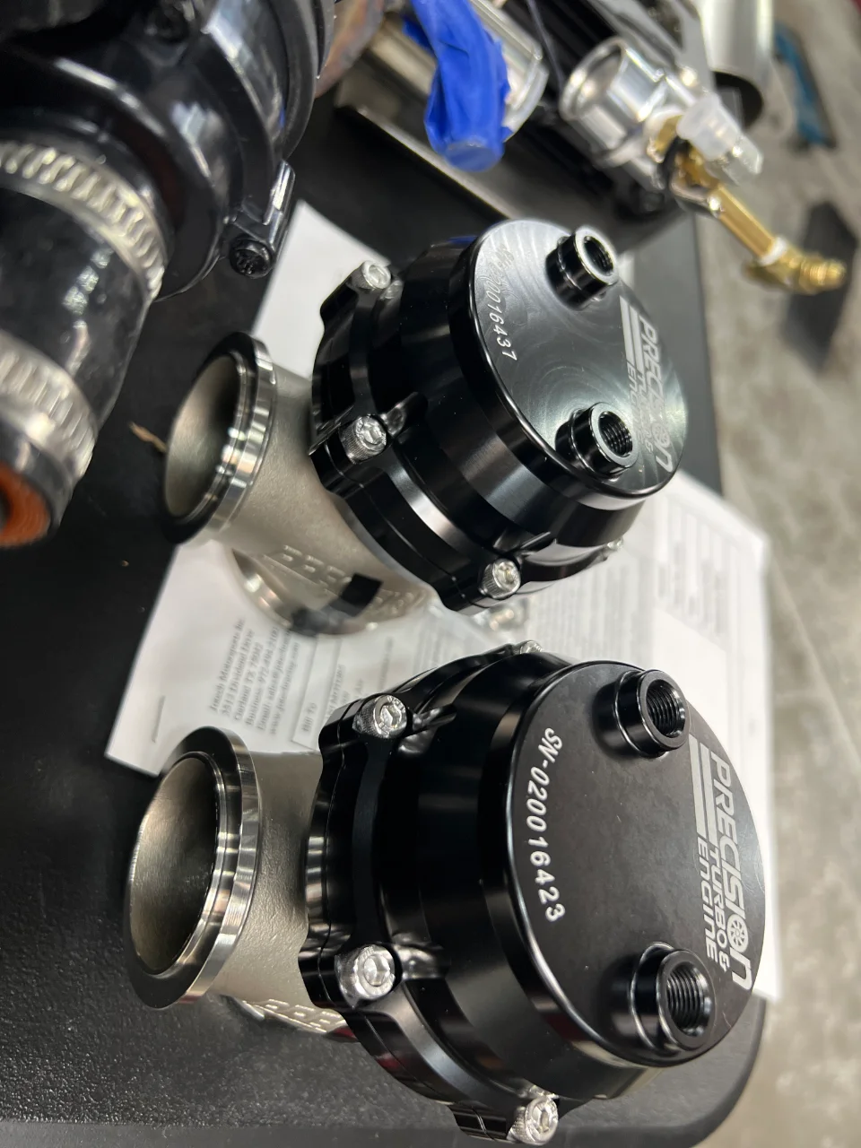 Two black Precision Turbo & Engine wastegates on a surface, ready for installation.