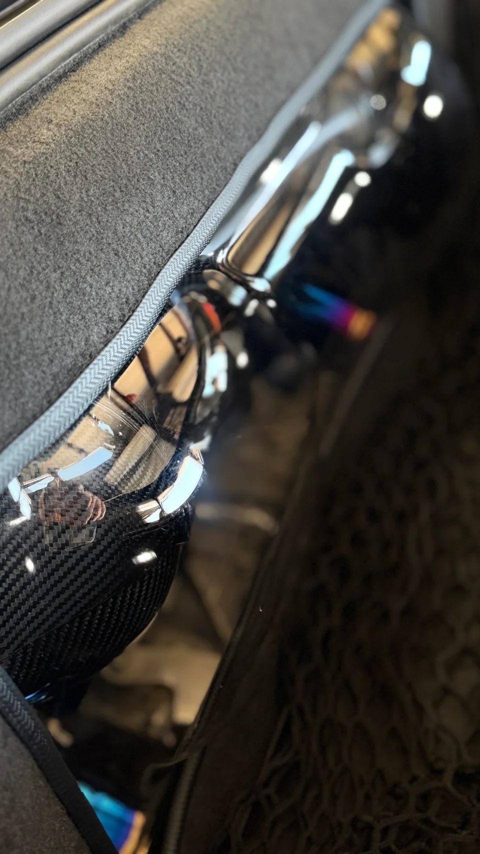 Close-up detail of a carbon fiber intake pipe with a reflective, possibly titanium, section and iridescent finish.
