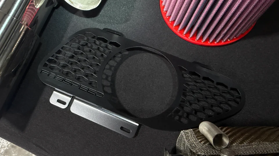 Fabspeed intake component with a performance air filter and metal piping on a black surface, showcasing car parts.