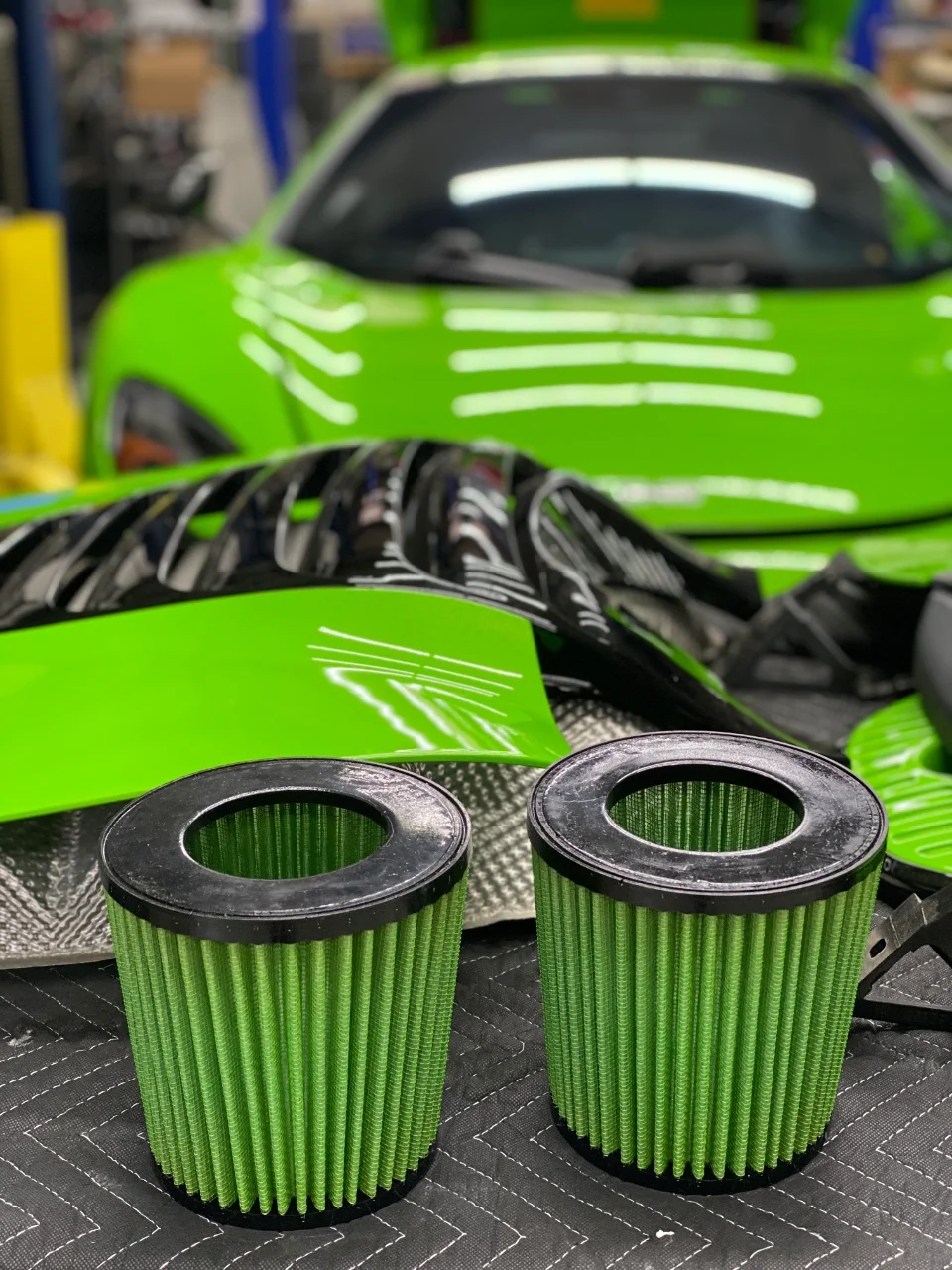 Two green performance air filters in a shop with a bright green McLaren in the background, ready for installation.
