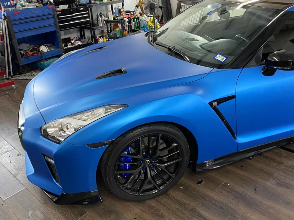 Matte blue Nissan GT-R with black wheels and blue calipers in a performance shop.