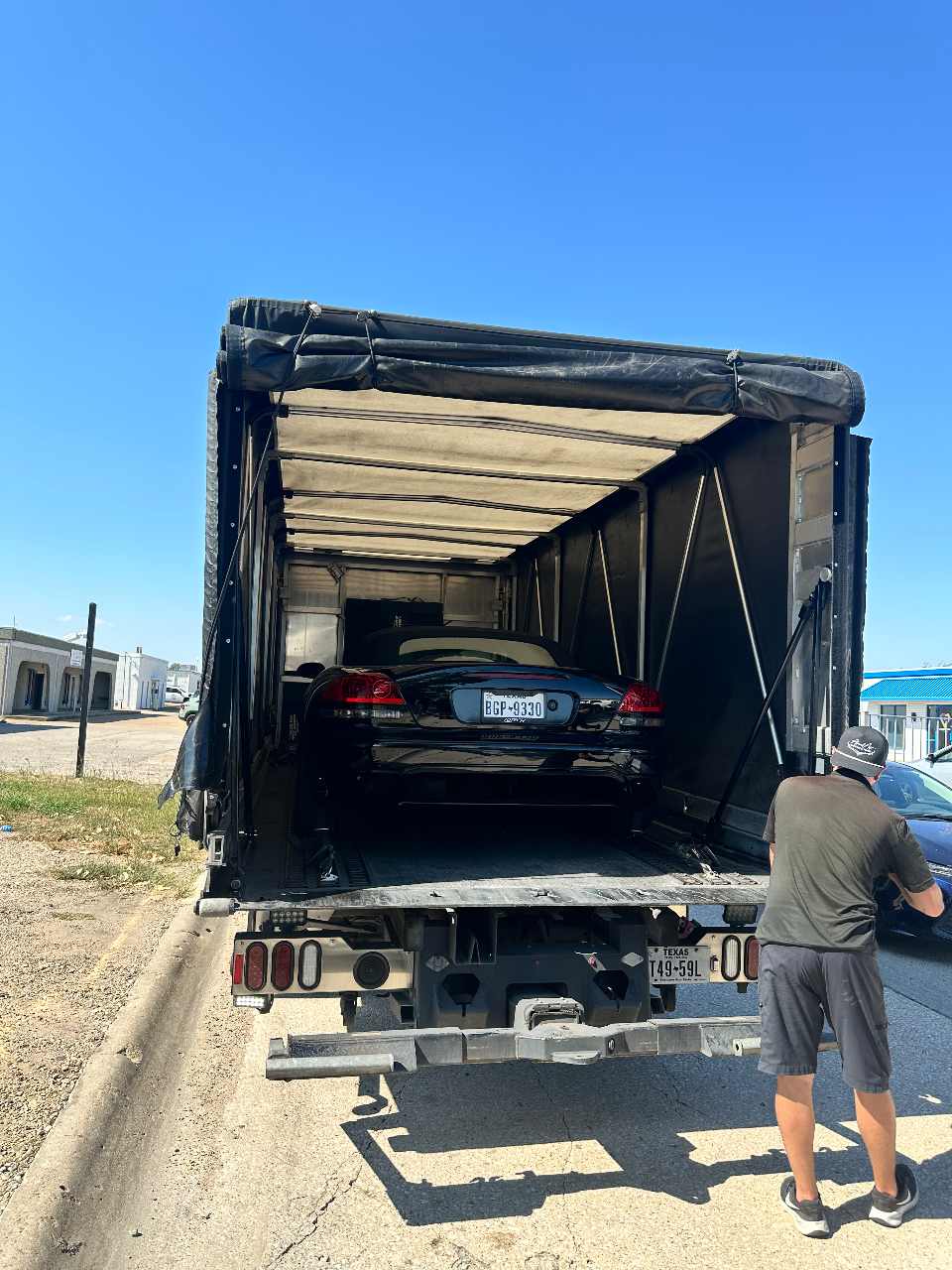 A black car with a Texas license plate being loaded into an enclosed car hauler, with a person standing at the rear.