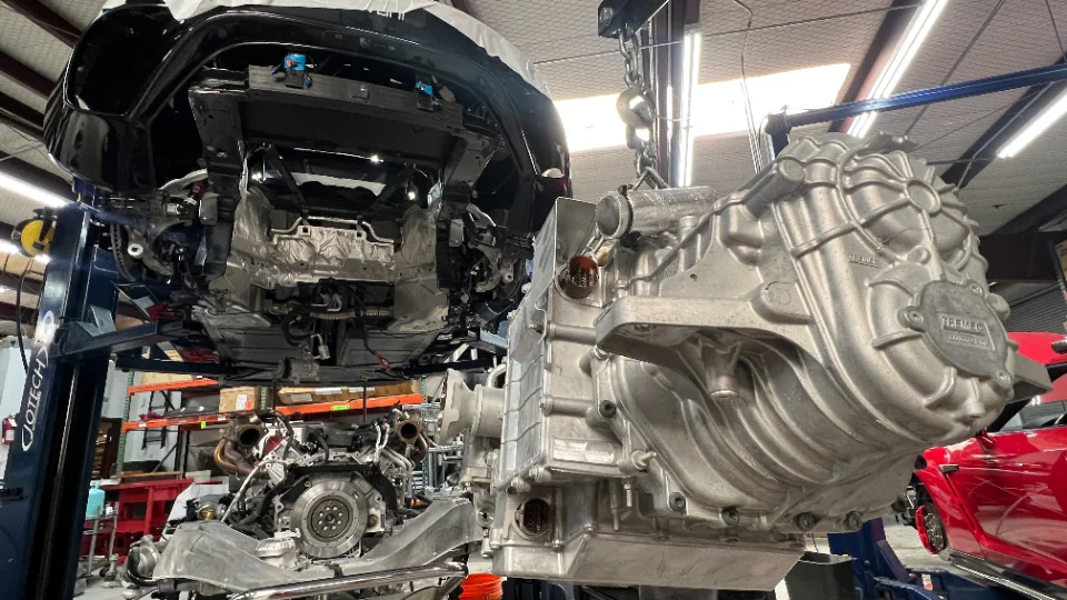 A car on a lift in a Jotech Motorsports shop with its transmission being removed or installed, showcasing the drivetrain.