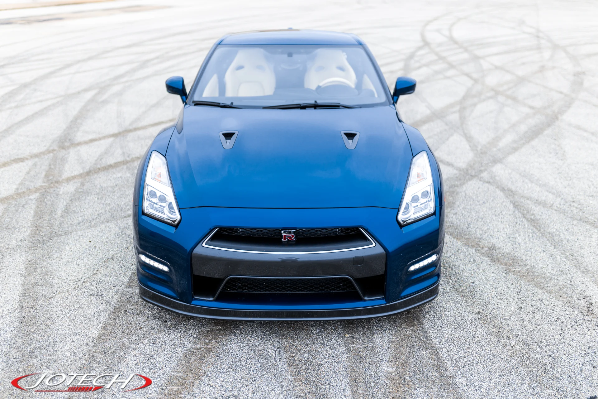 Front view of a blue Nissan GT-R parked on an asphalt surface with tire marks.
