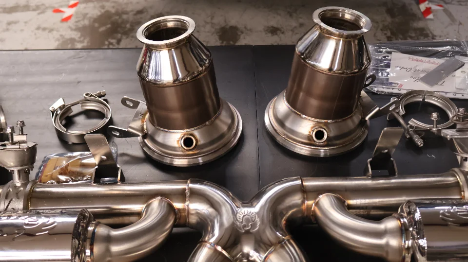 Close-up of new stainless steel aftermarket exhaust system components, including downpipes and an X-pipe, for a performance vehicle.
