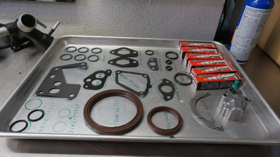 Various engine gaskets, seals, and HKS Super Fire Racing spark plugs laid out on a metal tray in a workshop.