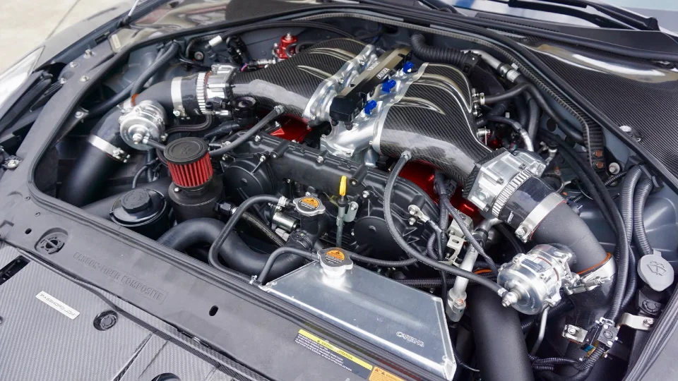A detailed view of a modified Nissan GT-R R35 engine bay featuring a carbon fiber intake manifold and aftermarket induction components.