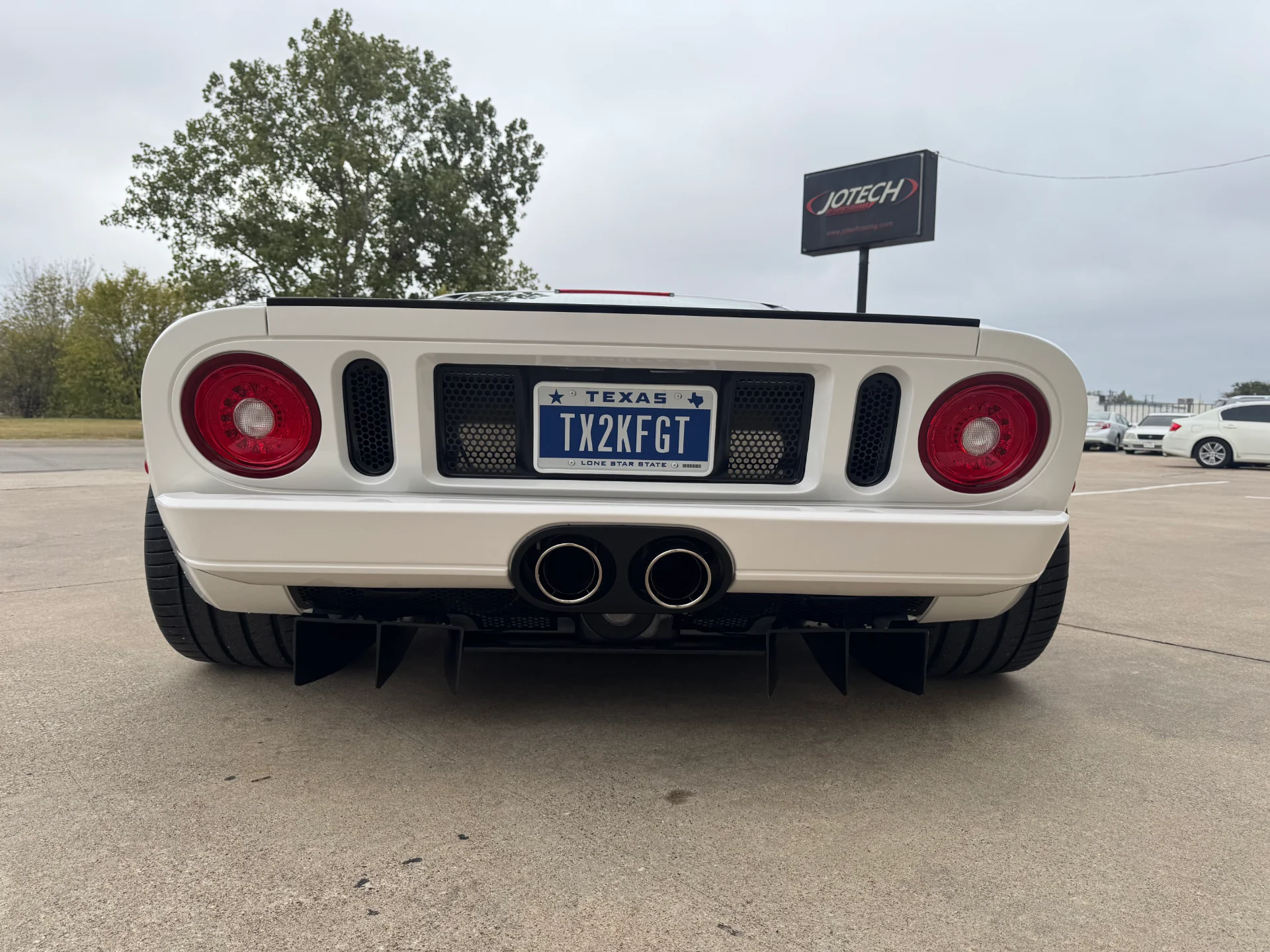 Rear view of a white Ford GT with a custom exhaust and rear diffuser, parked outside a Jotech facility.