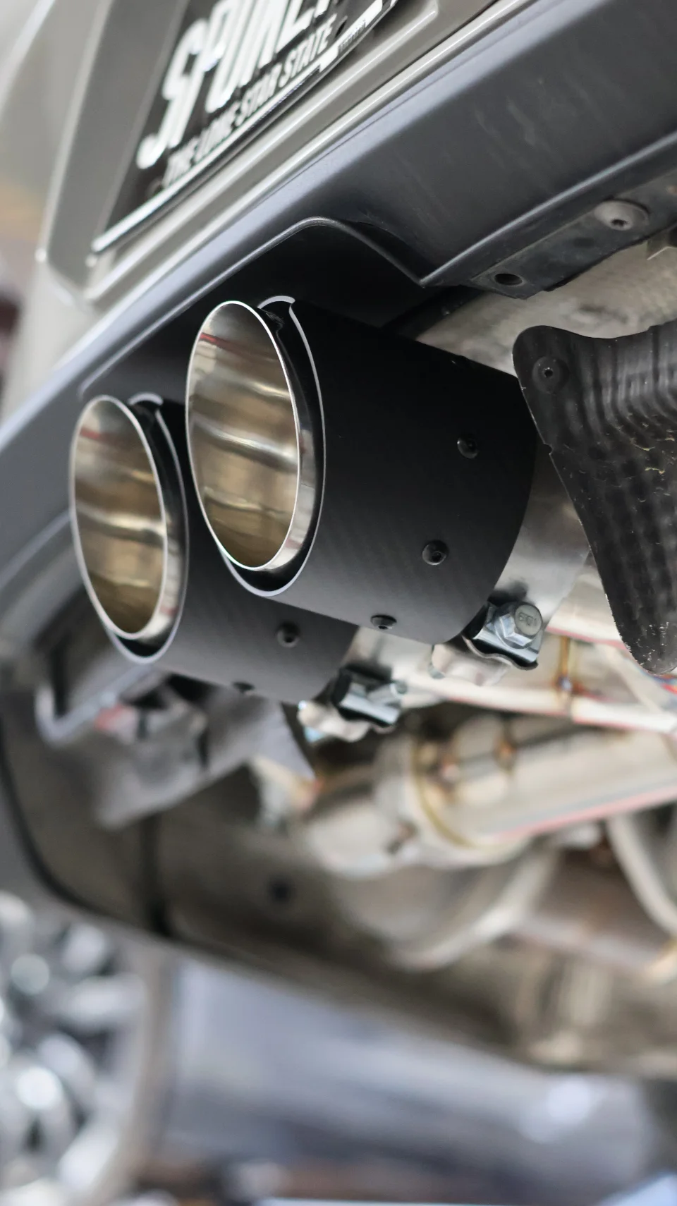 Close-up of a performance exhaust system with dual black and chrome tips on the rear of a car.