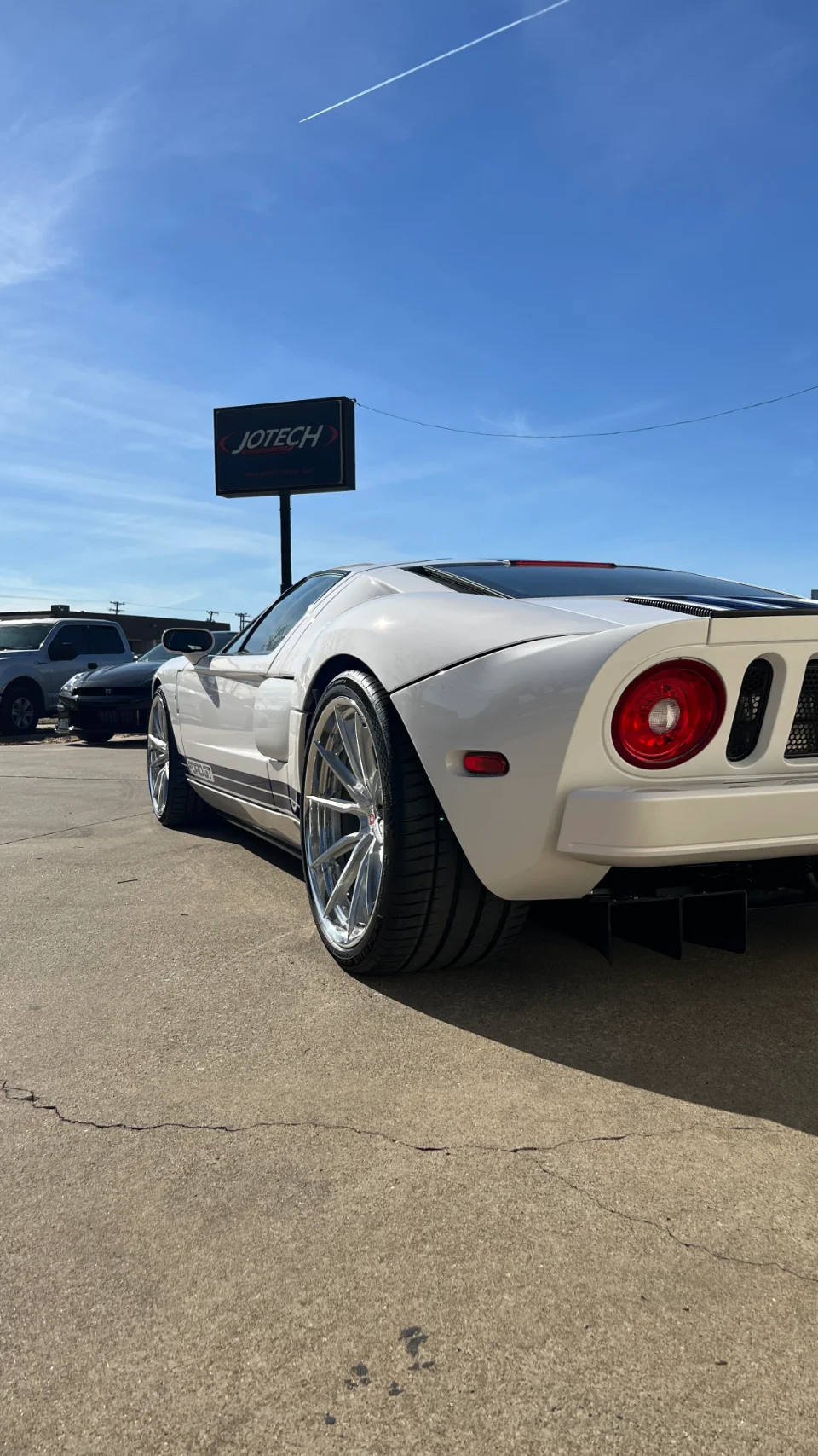 A white Ford GT with custom chrome wheels parked outside the Jotech Motorsports facility under a clear blue sky.