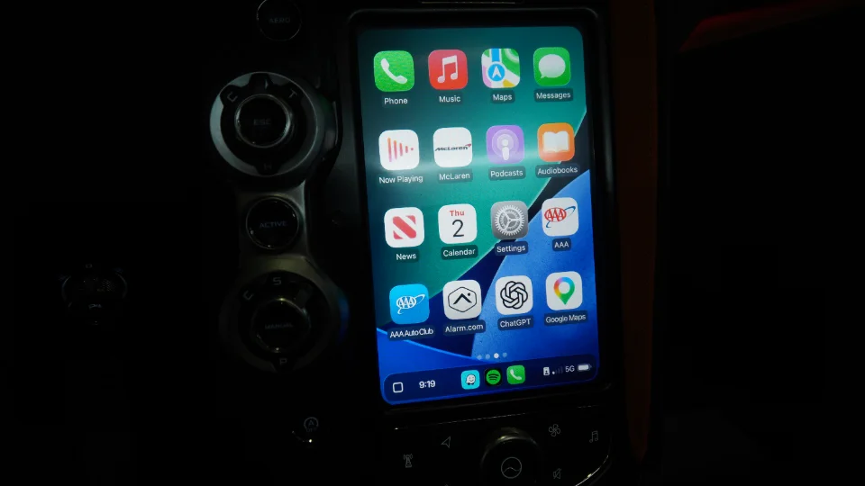 A smartphone screen displaying various apps, including McLaren, integrated into the dashboard of a McLaren supercar.