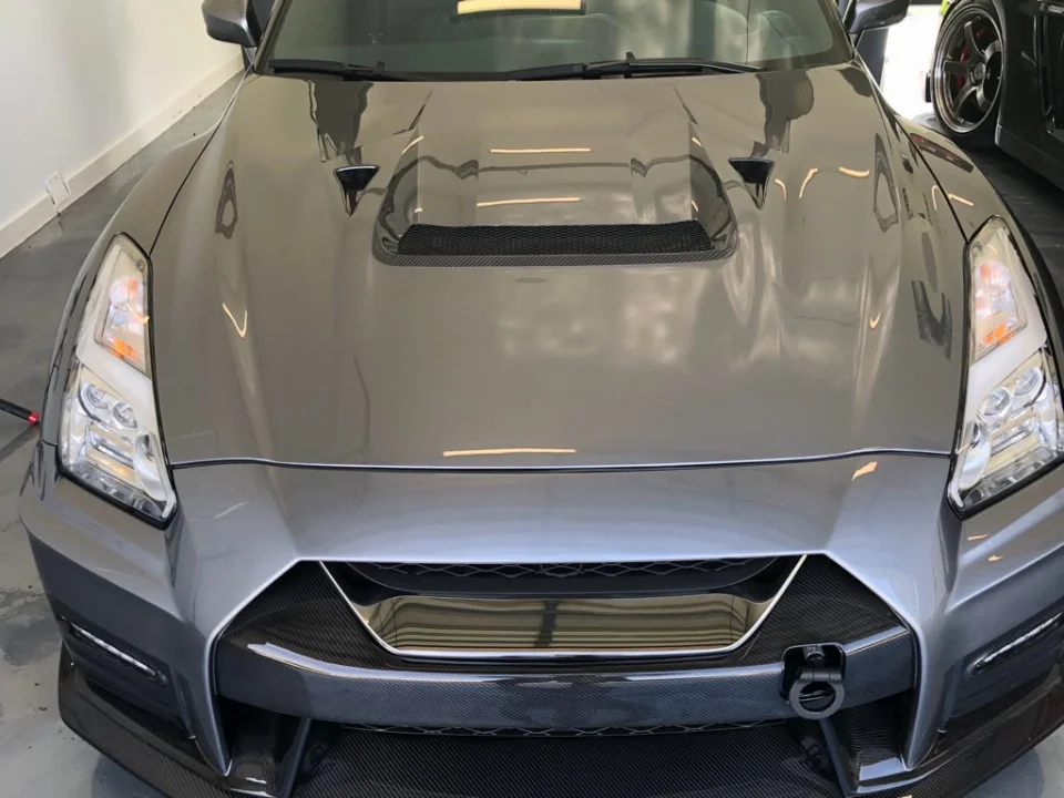 Front view of a grey Nissan GT-R with a carbon fiber hood and front bumper, showcasing its aggressive styling.